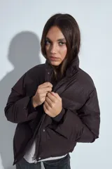 Campera puffer de nylon color marrón oscuro, con cuello alto, cierre frontal y puños elásticos. Diseño acolchado de volumen ligero.