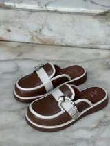 Zuecos negros de cuero con suela gruesa, detalle de tira de gamuza con hebilla metálica plateada y logo "AMÉN" estampado en la plantilla.