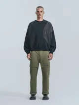 Buzo de cuello redondo, color negro, confeccionado en frisa gamuzada de algodón con recortes en microfibra, creando un efecto de capas. Presenta un bolsillo frontal tipo parche con cierre a presión.