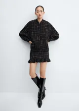 Minifalda negra de tweed con diseño a cuadros blancos, bajo asimétrico con volantes y cierre lateral con cremallera invisible.