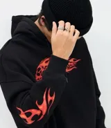 Buzo con capucha negro de corte oversized, con bolsillo canguro y cordones ajustables. Presenta un estampado frontal con una calavera y la palabra 'FEARLESS' envuelta en llamas naranjas y rojas, diseño que se repite en las mangas.