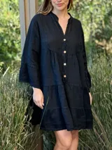 Vestido corto negro de lino con cuello mao y escote en V con botones de coco. Presenta mangas amplias con volados y un diseño escalonado con frunces en el busto y la falda.