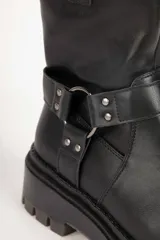 Bota estilo biker de cuero sintético color negro, con suela tipo plataforma dentada. Presenta una tira decorativa con argolla metálica y apliques de tachas en el tobillo.