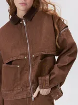 Campera de denim a rayas verticales con cuello de pana en color bordó. Presenta cierre frontal, mangas desmontables con cierre en los hombros, canesú en el pecho y bolsillos de parche cuadrados.