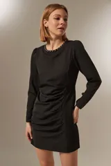 Minivestido negro de poliéster con mangas largas, cuello redondo con tachas plateadas, frunces laterales y corte ajustado.
