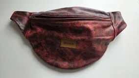 Riñonera de cuero color negro, de diseño suave y abombado, con cierre superior y etiqueta frontal con el logo de la marca.