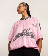 Remera rosa con cuello polo gris y rayas verticales. Estampado frontal con la palabra "gobline" en letras cursivas y la frase "in my best era". Diseño oversized con mangas cortas y recortes laterales en color negro.