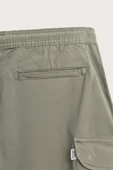 Bermuda cargo color negro de corte relaxed fit, confeccionada en tejido de algodón con elasticidad y efecto lavado. Cuenta con cintura elástica ajustable con cordón, bolsillos frontales y bolsillos laterales tipo cargo con solapa en las perneras.