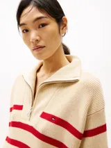 Sweater de punto color crema con rayas horizontales rojas, cuello alto con cremallera metálica y logo de Tommy Hilfiger bordado en el pecho.