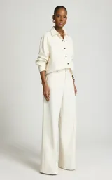 Pantalón sastrero de pierna ancha y tiro medio color marfil, confeccionado en algodón, con trabillas para cinturón, pliegues delanteros, bolsillos laterales y cierre frontal con cremallera y corchete.