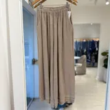 Pantalón ancho color beige, con cintura elástica fruncida, bolsillos laterales y detalles de costuras horizontales en los bajos.