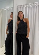 Top tejido con lurex, color negro con detalles plateados. Diseño halter con tiras cruzadas en el cuello y abertura en el centro del pecho.