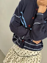 Saco de punto color crema con detalles en crochet verde, cierre frontal con botones y mangas largas.