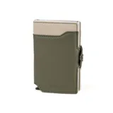 Billetera compacta de la colección Alabama de Baleine Co., confeccionada en símil cuero color verde y beige con estructura interna de aluminio. Cuenta con capacidad para 5 tarjetas con sistema de eyección mediante clip, compartimento para billetes, espacio para documentos y protección RFID.