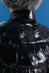 Campera puffer corta de color negro con acabado brillante, cuello alto y cierre frontal. Confeccionada en poliamida, presenta un diseño acolchado con bolsillos delanteros con cierre invisible.