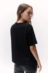 Remera negra de algodón con cuello redondo y manga corta. Presenta un calado en el hombro con detalle de pedrería.