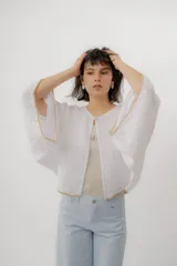 Blusa de lino color blanco, de diseño holgado, manga larga amplia acampanada con detalles de bordado en los puños y cuello redondo.