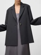 Blazer de corte recto y holgado en color gris melange, con solapas clásicas y cierre frontal de un solo botón. Presenta mangas largas y un diseño estructurado con detalles de costuras visibles.
