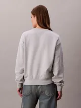 Buzo de felpa francesa gris claro, de cuello redondo y manga larga, con puños y dobladillo acanalados. Presenta un diseño holgado y lleva el logo retro de Calvin Klein bordado discretamente en el pecho.