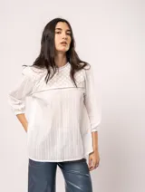 Blusa blanca de algodón con escote redondo, manga tres cuartos y silueta oversized. Presenta bordados y texturas combinadas.
