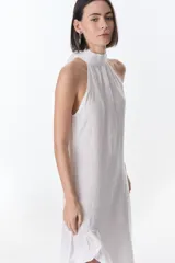 Vestido midi de lino italiano, color blanco, con cuello halter y diseño sin mangas. Presenta un corte recto y fluido con un detalle de volado en el ruedo.