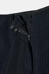 Pantalón de tiro medio confeccionado en mezcla de viscosa, con diseño de corte recto y largo tobillero. Presenta cintura con trabillas, bolsillos laterales, bolsillos traseros de vivo y cierre frontal con cremallera, botón y ganchos metálicos. El diseño incluye un sutil estampado de rayas verticales.