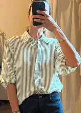 Camisa a rayas verticales verdes y blancas, de manga larga abullonada con puños elásticos y cuello camisero clásico.