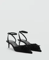 Zapato tipo kitten heel color negro, con punta fina y detalle de pompones en el empeine. Cuenta con una tira ajustable con hebilla en el tobillo.