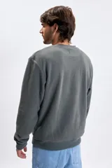 Buzo de polar gris oscuro con cuello redondo, mangas largas y puños elásticos. Presenta un estampado minimalista con la frase 'coming soon' en el centro del pecho.