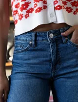 Jean de tiro alto, color azul medio, con pierna ancha y terminación de ruedo desflecado. Presenta cierre y botón en la pretina con pasadores, y bolsillos delanteros y traseros.