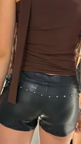 Short negro de tiro bajo confeccionado en cuero sintético, con cordones cruzados ajustables al frente y detalles de tachas metálicas en los bolsillos.