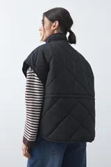 Chaleco acolchado de nylon con diseño capitoneado, cuello alto y cierre frontal con botones a presión. Presenta un calce amplio y versátil.