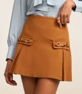 Minifalda marrón de polivelour con cierre lateral, solapas con hebillas y pliegues.