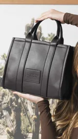 Cartera estructurada de tamaño mediano, confeccionada en símil cuero color negro. Presenta doble asa de mano, correa larga ajustable y desmontable, y un bolsillo trasero con cierre. El compartimento principal cuenta con cierre, división interna y bolsillos organizadores.