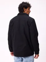Campera de gabardina negra, con cuello camisero, cierre frontal de cremallera y botones a presión. Posee múltiples bolsillos frontales con solapa y puños ajustables con botones.