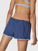 Short deportivo 2 en 1 color azul con detalles en celeste, que incluye calza interior incorporada. Presenta una cintura ancha de tiro alto en color tostado, con diseño de bordes redondeados y costuras a contratono.