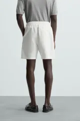 Bermuda de algodón color beige claro, de corte regular fit, con cintura elástica ajustable mediante cordón. Presenta bolsillos laterales y un bolsillo trasero de vivo.