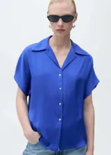 Camisa azul eléctrico de tejido satinado, manga corta, cuello camisero y cierre frontal con botones. Corte regular.