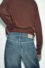 Jeans de tiro bajo, corte recto y largo completo (full length), color azul medio con efecto desgastado y lavado. Modelo de cinco bolsillos con cierre frontal de botones.