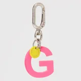 Llavero con dije en forma de letra A color rosado y pequeño dije circular amarillo con logo de la marca grabado. Incluye gancho metálico tipo mosquetón.
