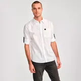 Camisa de manga larga convertible, color blanco, confeccionada en popelina. Cuenta con cuello clásico, cierre frontal con botones, bolsillo en el pecho con etiqueta de marca y mangas enrollables con pestaña de ajuste.