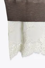 Vestido de punto marrón oscuro, sin mangas y cuello redondo, con un ruedo inferior de encaje blanco.