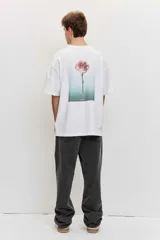 Remera blanca de manga corta, corte oversize, con estampa en la espalda de una flor sobre fondo difuminado verde y blanco.
