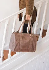 Bolso de mano tipo shopper marca Amadea, confeccionado en cuero con acabado desgastado. Presenta detalles de costuras decorativas verticales, correas con hebillas metálicas doradas y logo grabado al frente.