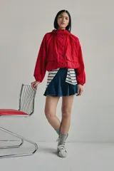 Campera parka roja estilo blouson con capucha ajustable, cierre frontal de botones a presión, bolsillos frontales con solapa y diseño holgado.