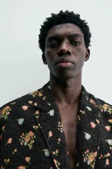 Blazer de hombre de corte relaxed fit confeccionado en tejido jacquard negro con estampado floral multicolor. Tiene cuello con solapas de muesca, manga larga con puños abotonados, bolsillo de vivo en el pecho, bolsillos de solapa en la cadera, bolsillo interior, abertura en el centro de la espalda y cierre frontal con botones.