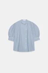 Camisa de algodón con estampado de rayas verticales azules y blancas. Presenta cuello mao, cierre frontal con botones a contraste y mangas cortas abullonadas con puños rectos.