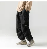 Pantalón cargo negro, de corte ancho y holgado, con múltiples bolsillos tipo parche en las piernas. Presenta un pequeño logo blanco de montañas en el bolsillo lateral. El tejido parece ser ligero e impermeable, con ajuste elástico en la cintura y tobillos.