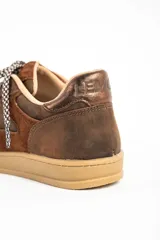 Zapatilla urbana de cuero en tonos marrones, con paneles de gamuza y detalles metalizados en el talón. Presenta cordones bicolores y suela de goma al tono.