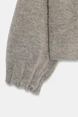 Chaqueta estilo bomber de punto color gris, con cuello subido, manga larga y acabados elásticos con frunces en puños y cuello. Cierre frontal con botones a presión ocultos.
